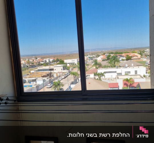 חלון הזזה מאלומיניום כהה עם רשת המציג נוף פתוח